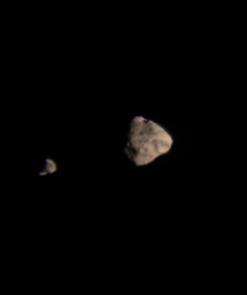 slightly blurry image of brown asteroid with smaller same to the left of it against blackness of space