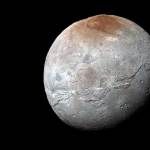 A full glove view of Pluton's moon, Charon. The moon is gray with a reddish cap.