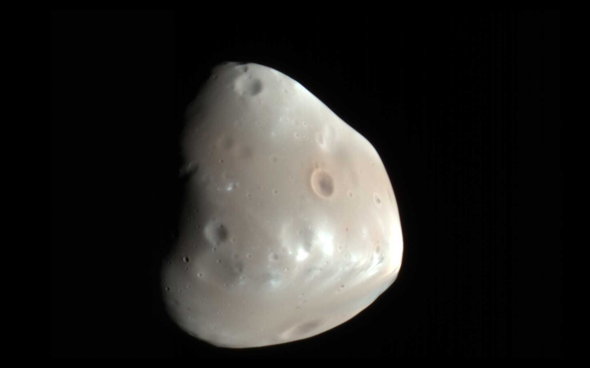 A color-enhanced image of Mars' moon Deimos. Deimos has a smooth surface except for the most recent impact craters. It is a dark, reddish object.
