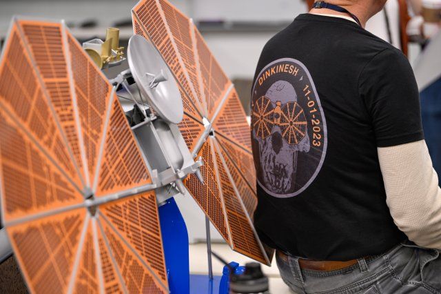 A team member sits with their back to a large model of the Lucy spacecraft with its large, circular solar panel arrays. Image credit: Lockheed Martin
