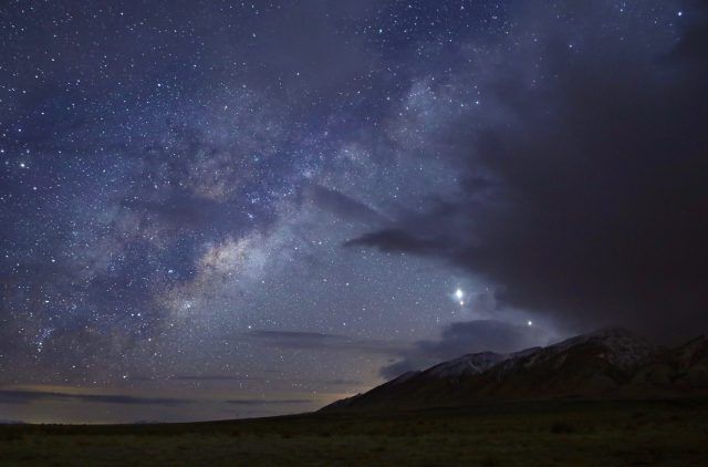 Stars in the night sky over a darkened Earth landscape.