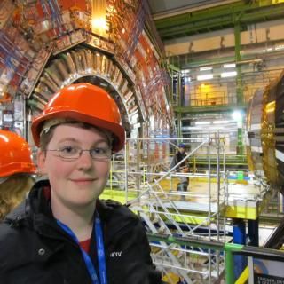 Photo of a smiling woman wearing an orange hard hat and standing in a lab