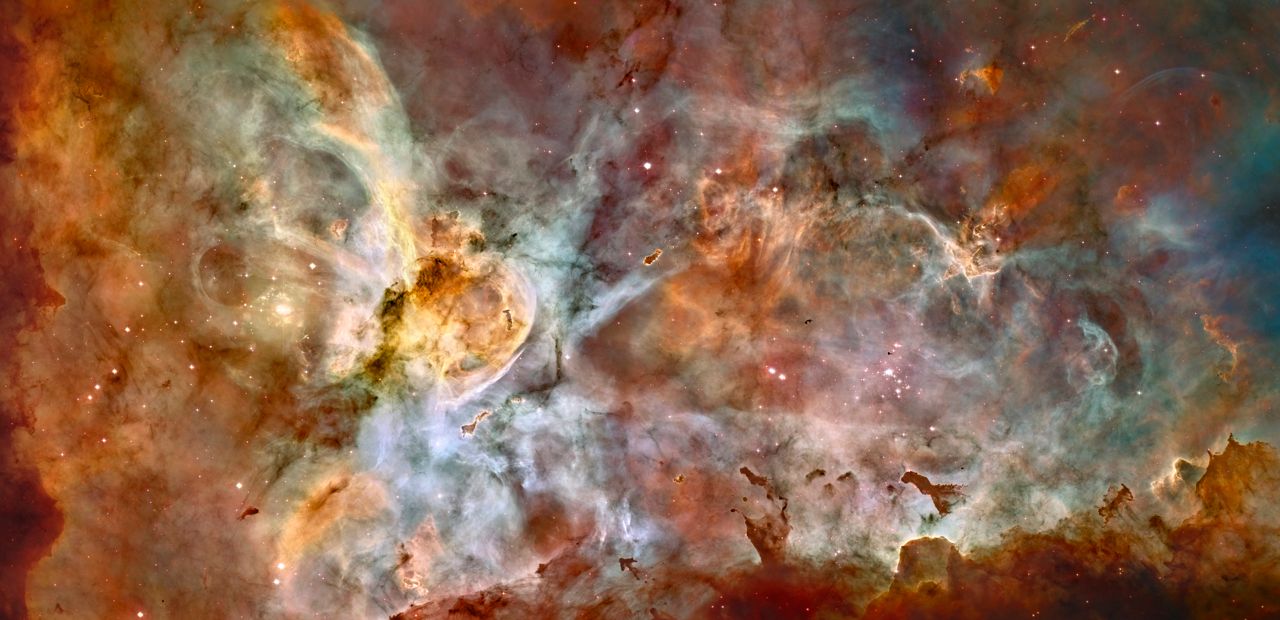 Entire image is filled with green, brown, rusty colors of the Carina Nebula. Chaotic groupings of this dust and gas with stars dispersed randomly throughout the image.