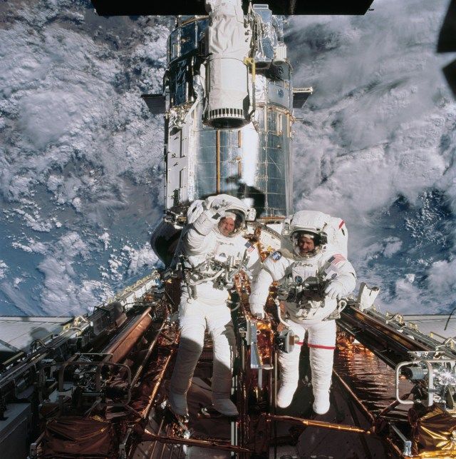 Two astronauts float in the cargo bay in bright sunlight.