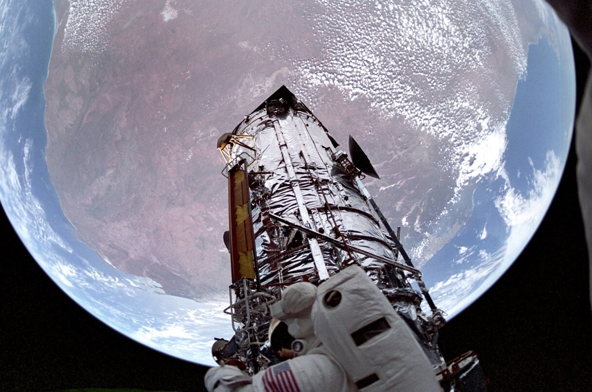 Earth in the background, Hubble in the foreground, and an astronaut at the bottom of Hubble.