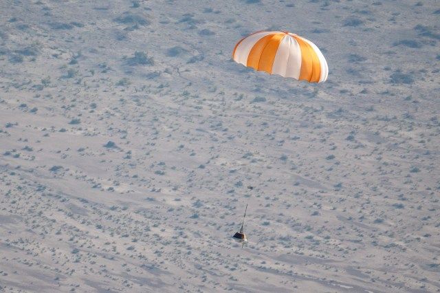 Image of practice sample return capsule attached to a parachute landing in the Utah Testing and Training Range during the practice sample return.