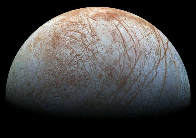 A half disc view of Europa shows crisscrossed lines on the icy surface.