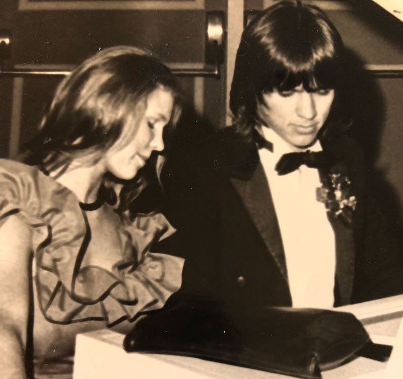 Lori Glaze and her future husband sitting together at a piano at their senior prom.