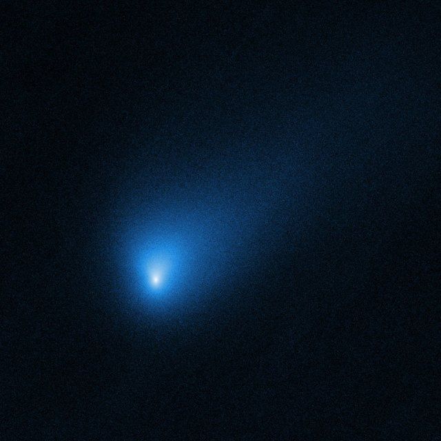 bluish comet trailing dust and gas as it travels through space.
