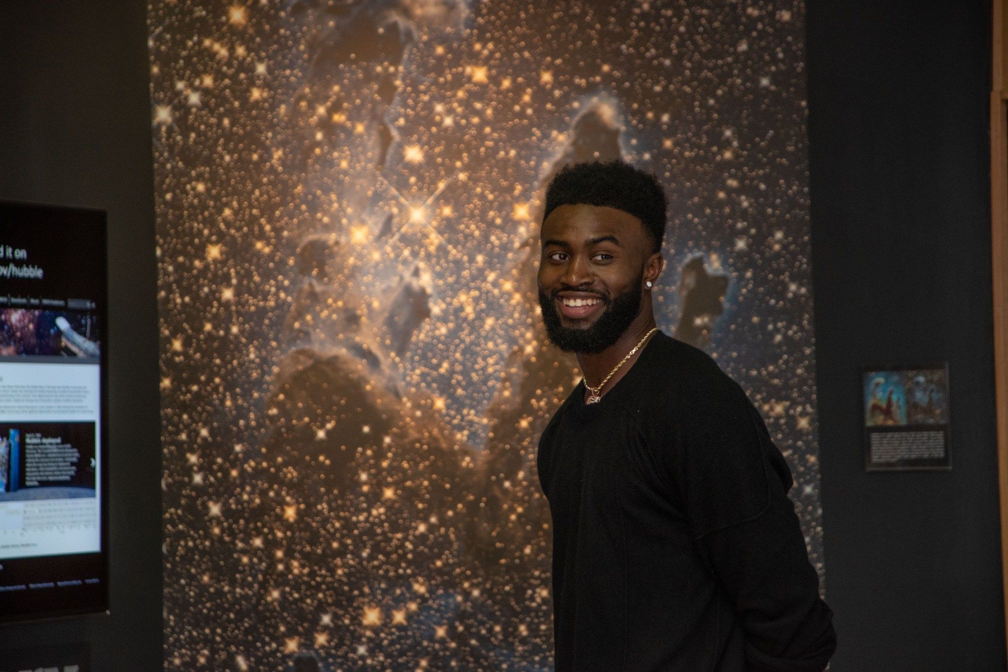 NBA star Jaylen Brown smiles in front of an infrared image of the Eagle Nebula showing a myraid of stars.