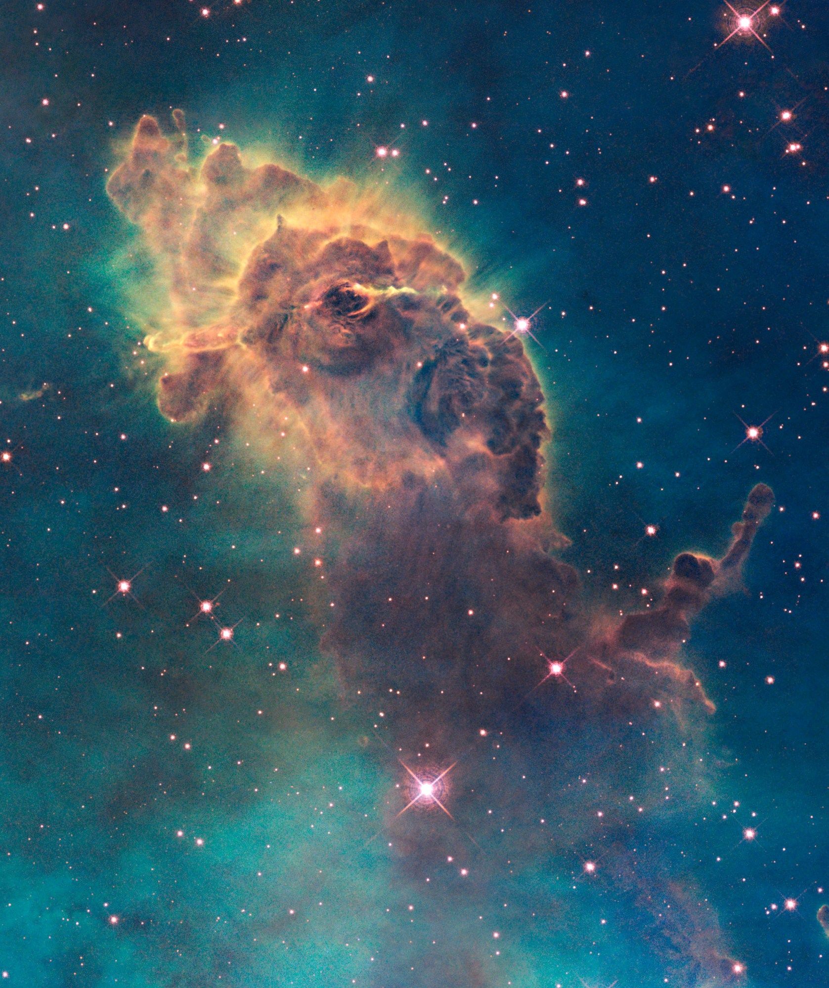 An orange and brown pillar of gas and dust rears up against a blue background dotted with pinkish stars. The pillar is brighter and more distinct toward the top and dimmer and more diffuse toward the bottom. Gas is streaming off the top of the pillar.