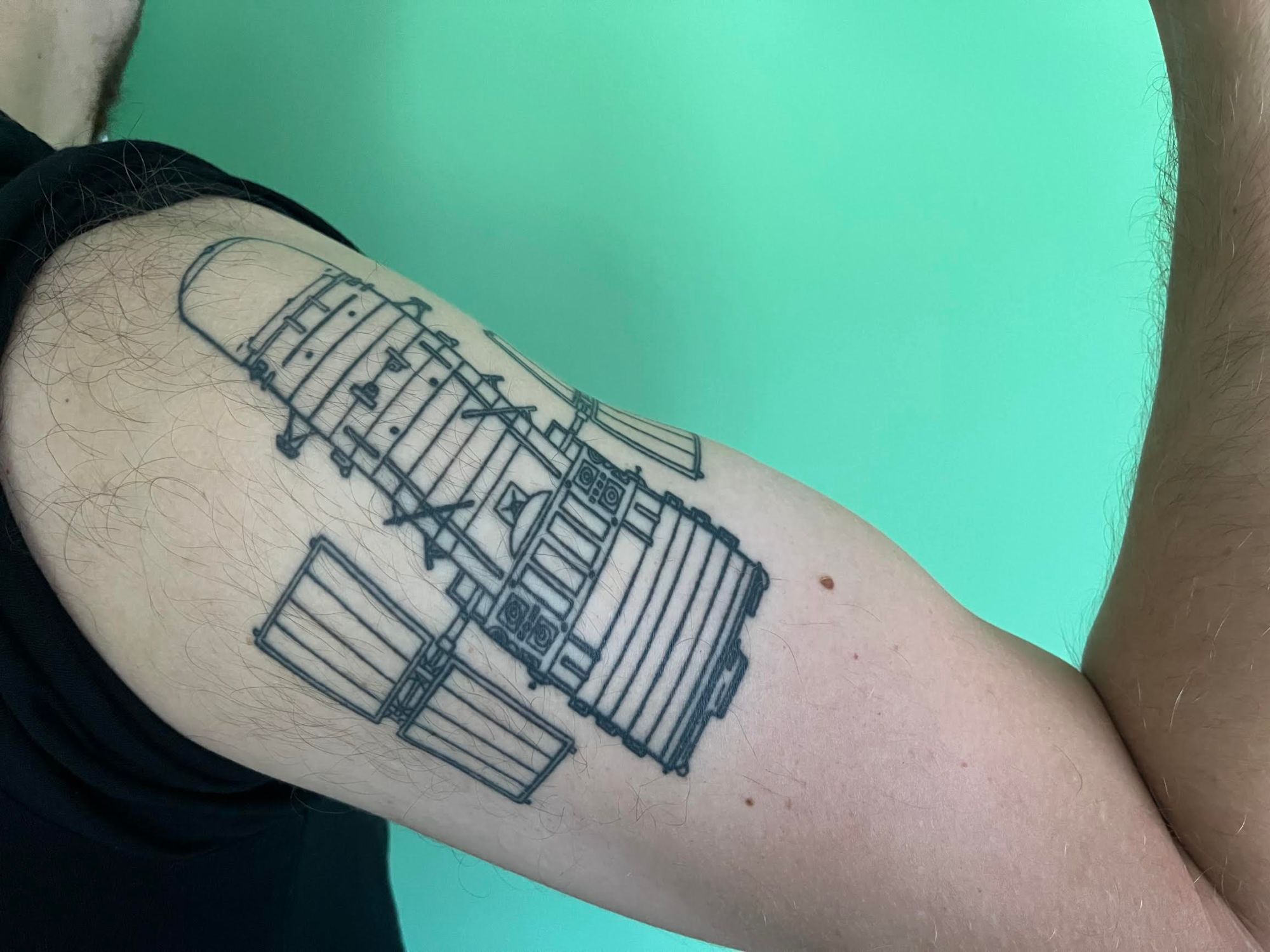 An arm tattooed with a blueprint-like image of the Hubble Space telescope.