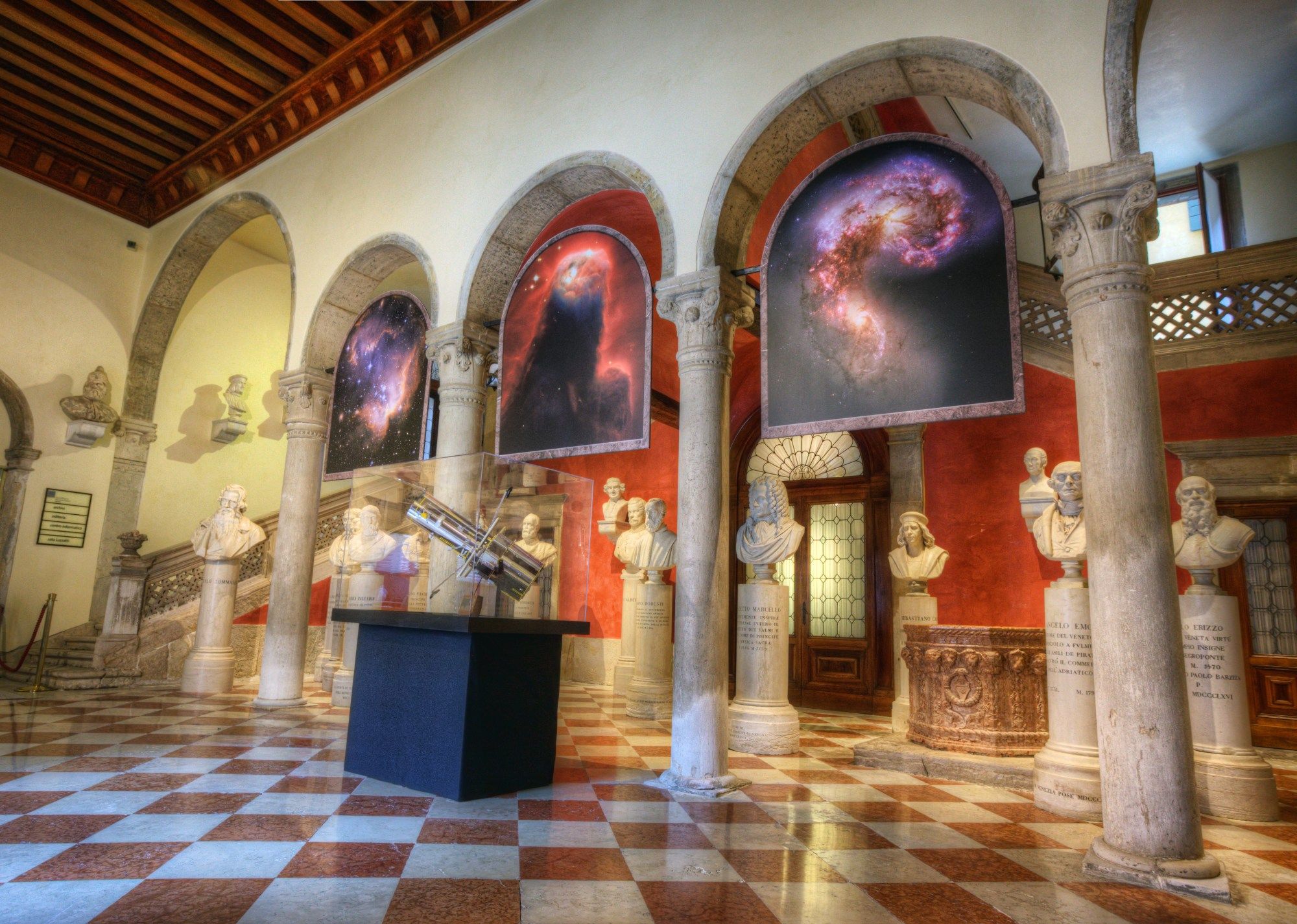 Hubble images are suspended between stone arches and hanging over classical marble busts at an art museum. A Hubble model is displayed among the statues.