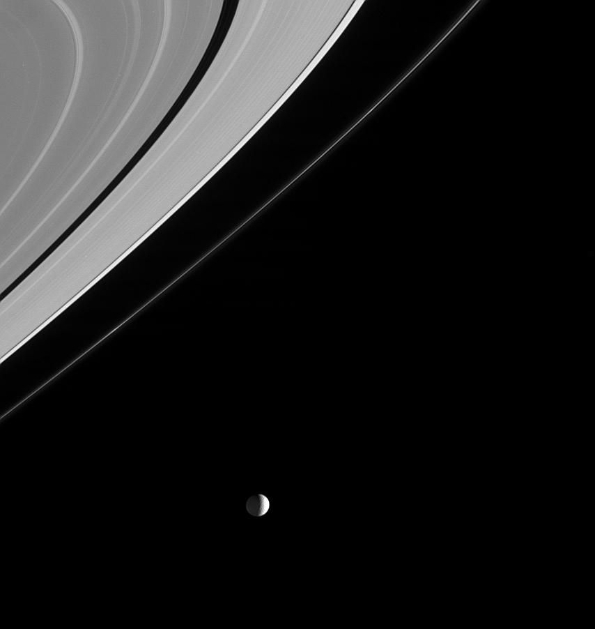Black and white image of Mimas to the left of Saturn's rings.