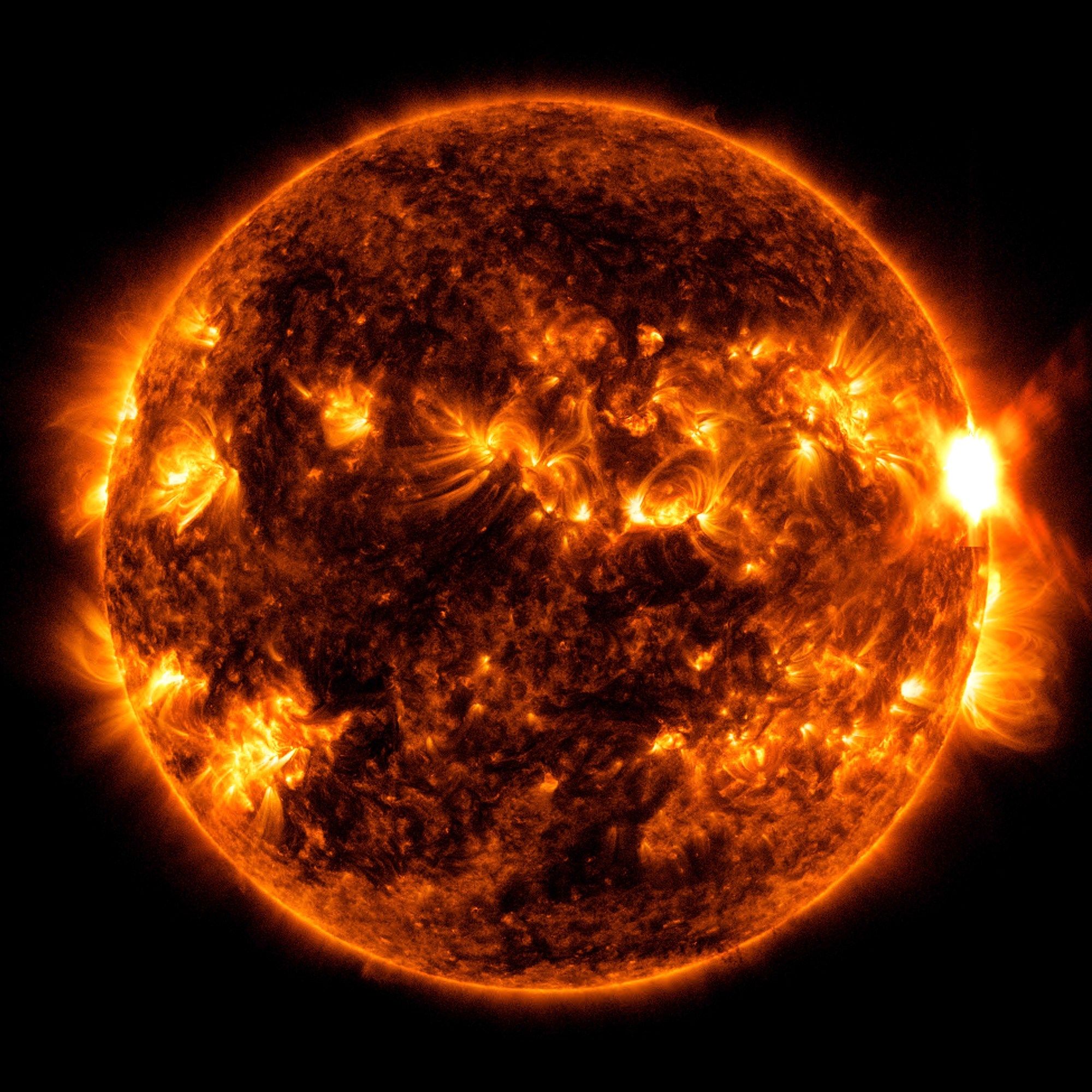 The Sun shown in red and orange, swirled with darker inactive areas and brighter active areas. On the right side of the Sun, there is a very bright region where the flare erupts.