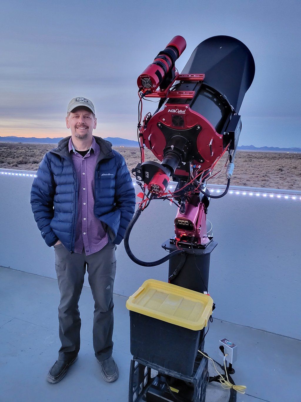 A man standing next to a large telescope with the sky in the background