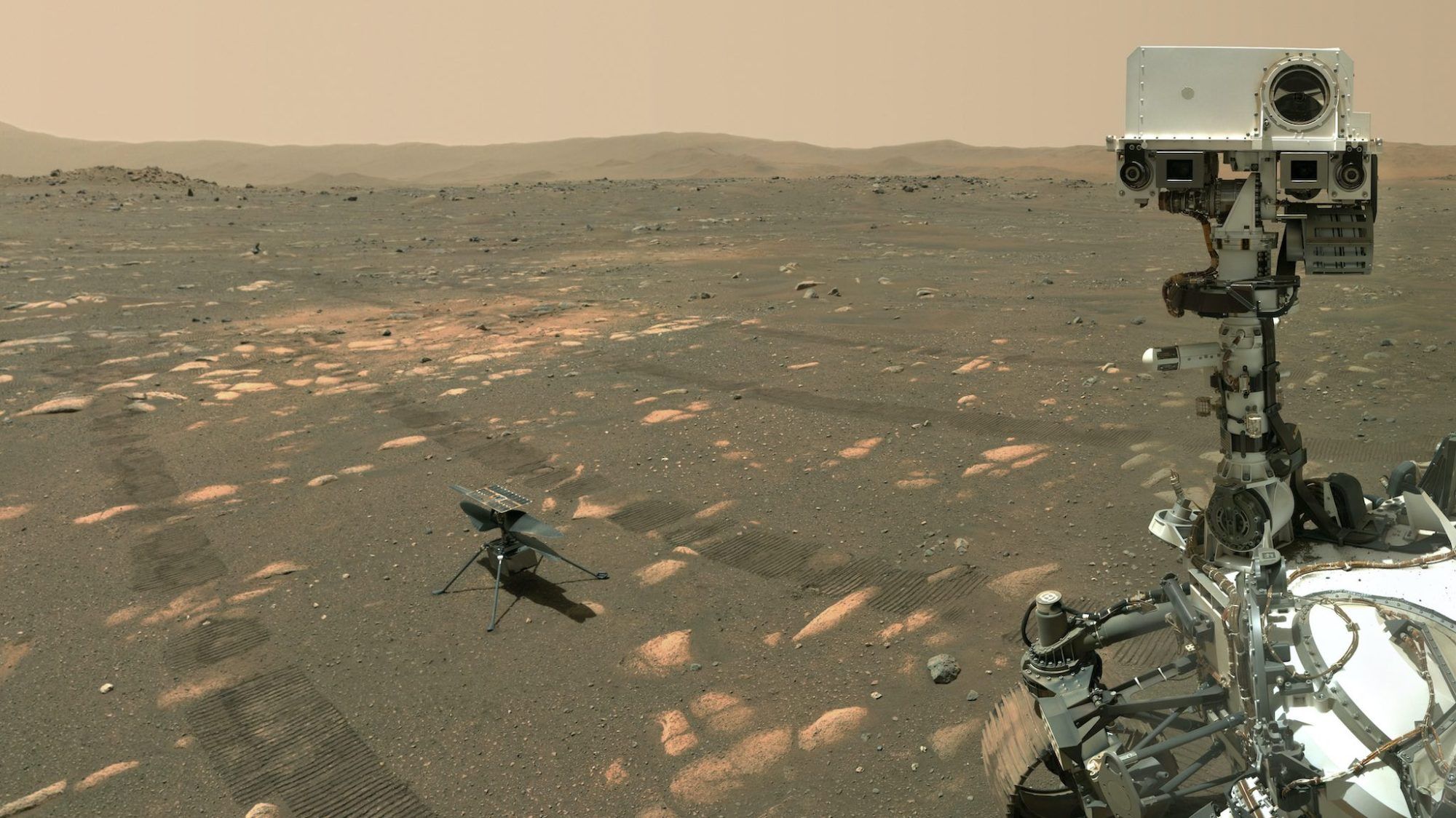 A small helicopter sits on the surface of Mars near the much larger Perseverance rover.