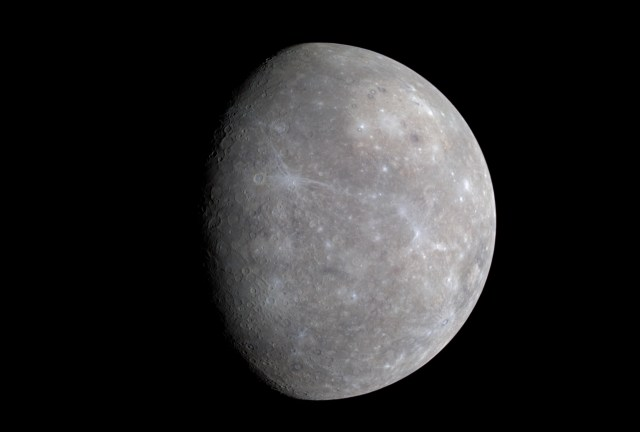 Within the light gray of Mercury's surface are splatters of pale blue, as the left side of the planet is in shadow.