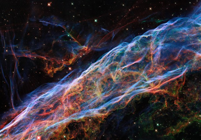 Colorful wisps of dust and gas appear diagonally from lower left to upper right ot the image, set against the black backdrop of space.