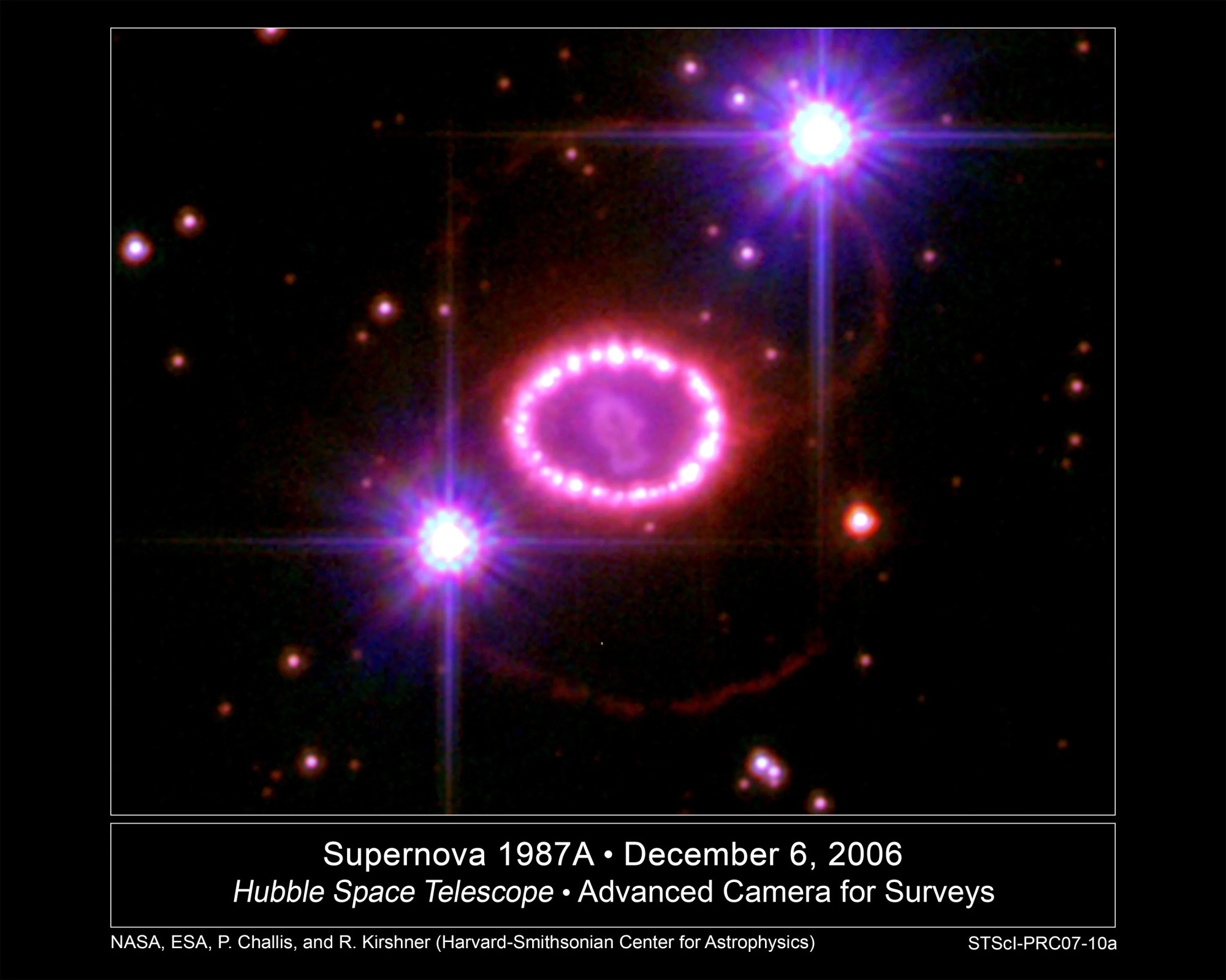 A string of pinkish pearls surrounds an exploded star. Black background dotted with stars. Two bright stars, with diffraction spikes, at lower left and upper right of the ring.