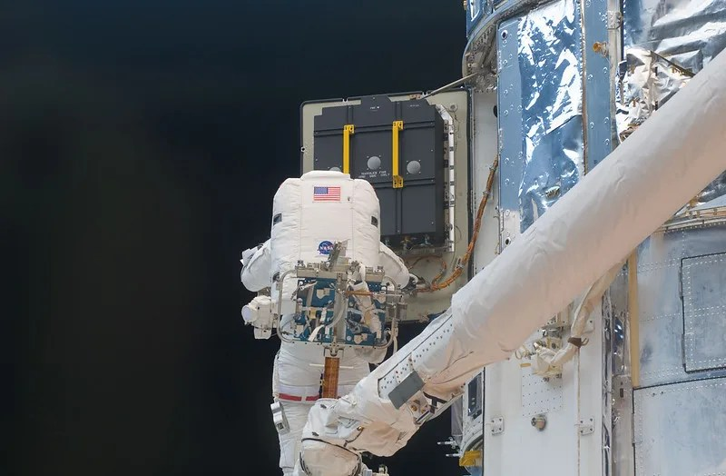 Astronaut in a white suit on a white mechanical arm replacing equipment