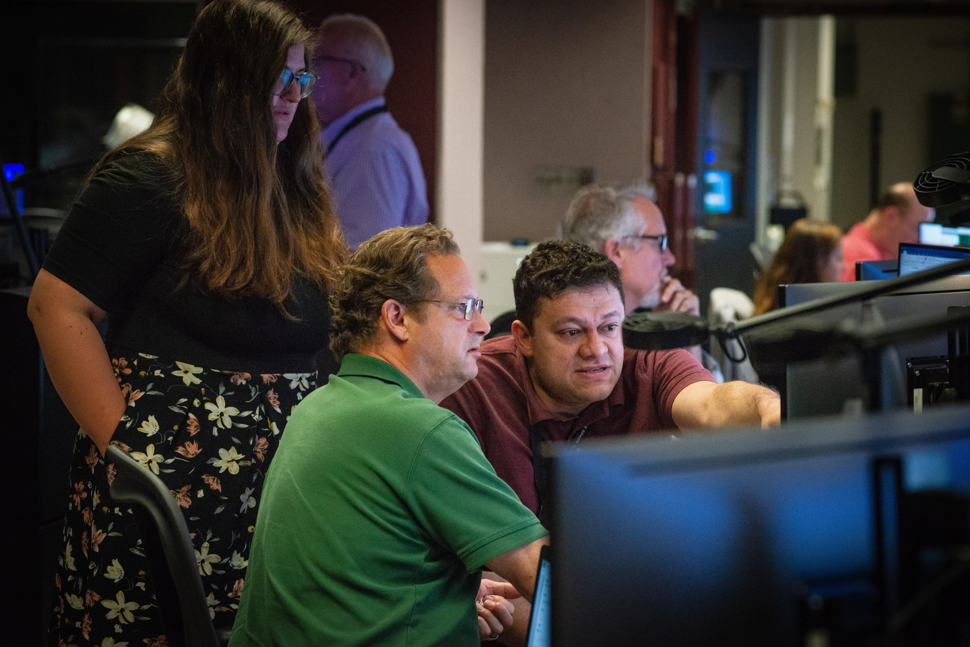 Three people discussing spacecraft operations in the control room for the Hubble Space Telescope.