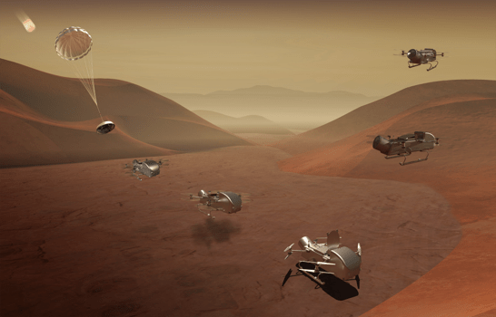 A group of silver spacecraft flying over and landing on a sandy brown surface is shown. An inflated parachute with an oval-shaped capsule below it is shown descending at the left. Sandy dunes are shown in the background.