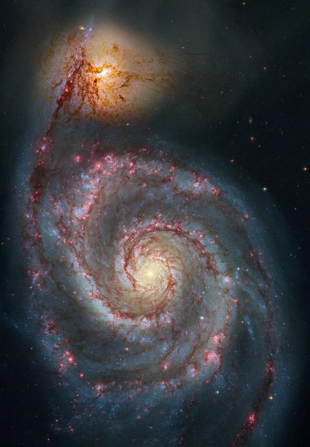a large, face-on spiral galaxy fills the image. It's bright core is surrounded by pinkish-red dusty spiral arms