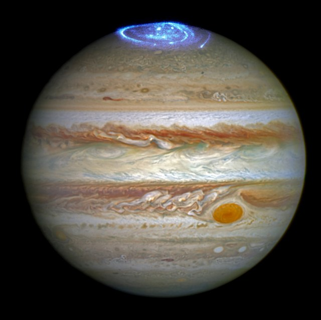 Jupiter with its rusty-orange, red, white, yellow, and tan horizontal cloud bands on a black background. The red spot is located in the lower-right quadrant of the image near image center. At the top of the planet is a swirl of light blue light.