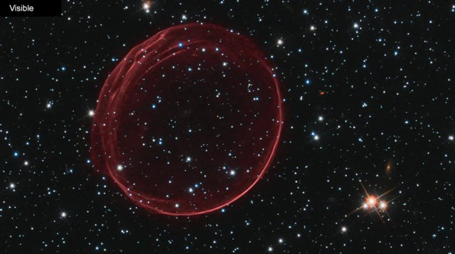 Black background dotted with stars. A dark-red transparent bubble of gas looking like a ring. Stars are visible through the center of the ring.