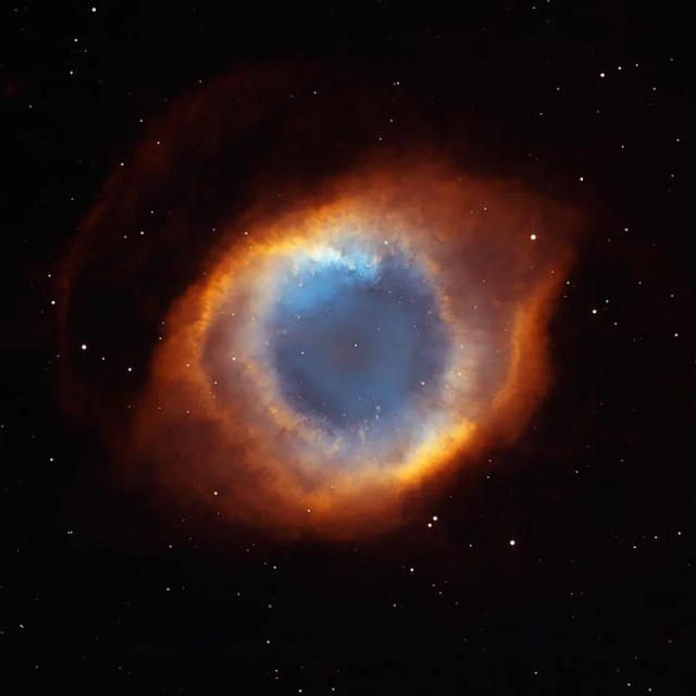 Black background. At image center is a colorful ring of gas and dust. The ring is a deep red along the outside. Moving inward toward the center of the ring, the colors change from red, to orange, to yellow, to pinkish-white, to a light blue sphere in the center.