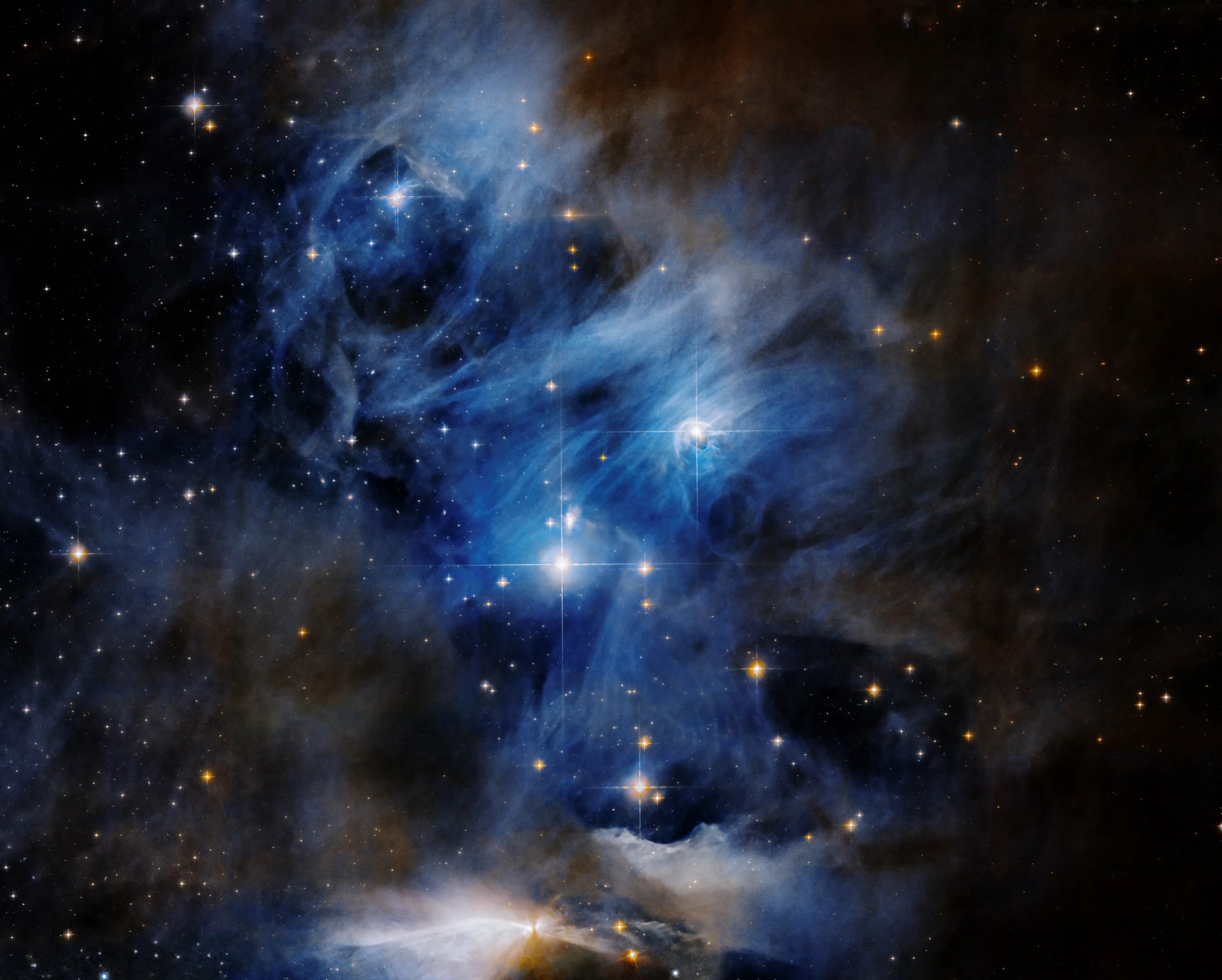 Bright blue and white nebula with bright young blue stars dotted through the image. bottom center: herbig-haro object, bright white clouds extend left and right, center point is white with rusty margins