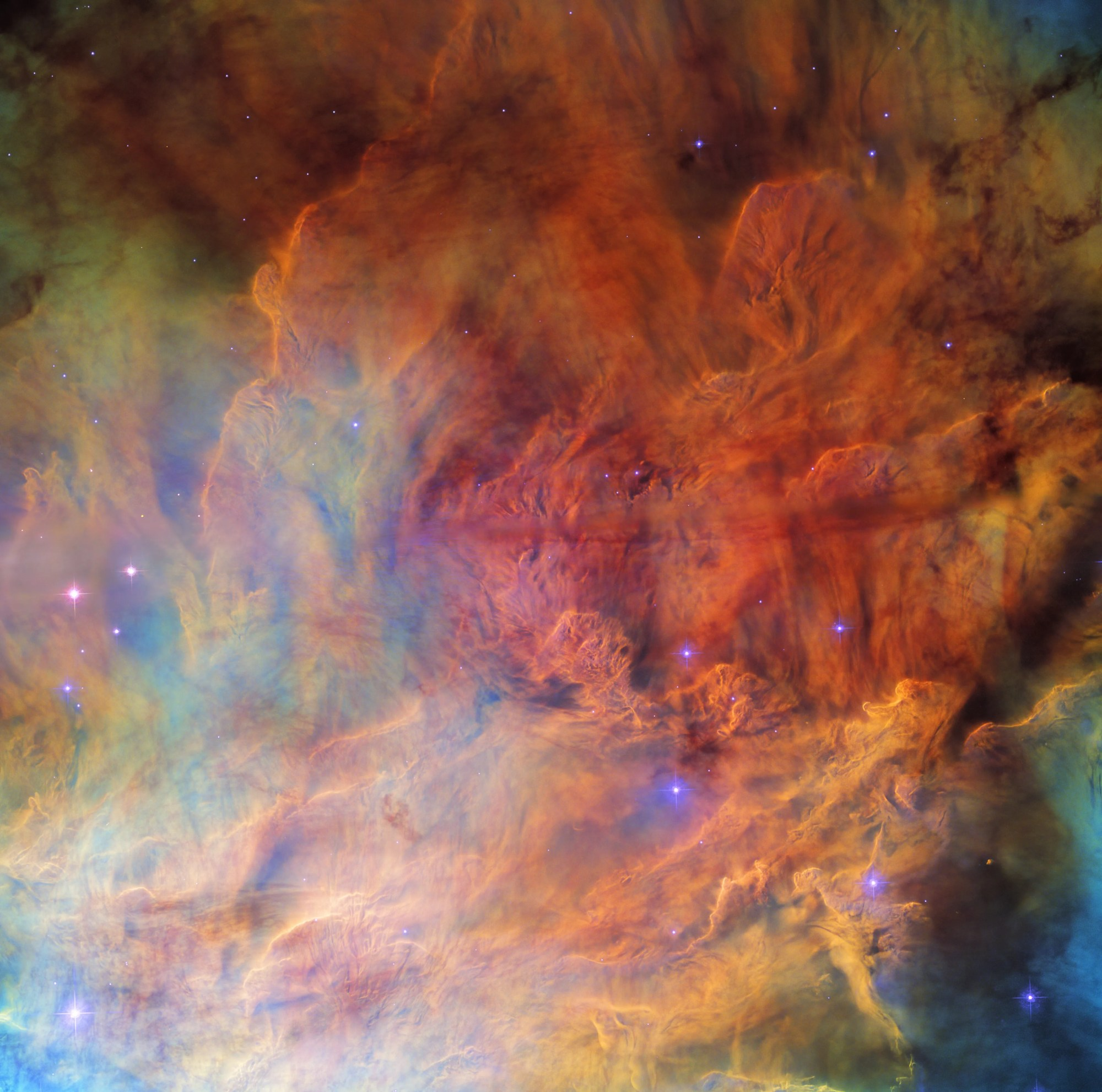 Clouds of gas cover the entire view, in a variety of bold colors. in the center the gas is brighter and very textured, resembling dense smoke. around the edges it is sparser and fainter. several small, bright blue stars are scattered over the nebula.