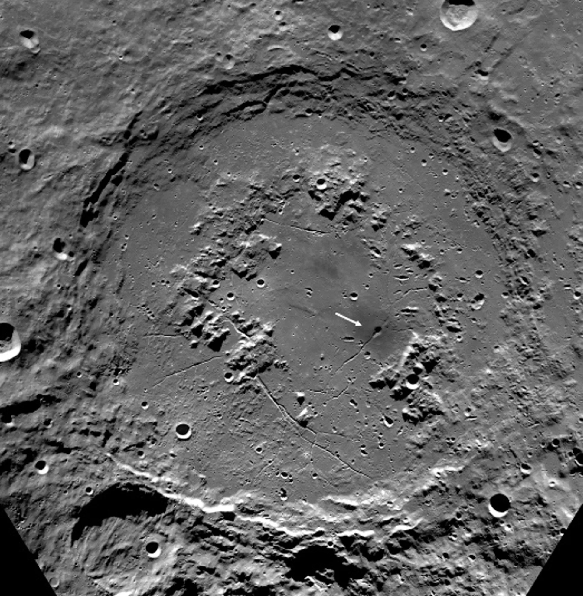 The image is zoomed in on the lunar impact crater known as Schrödinger Basin, appearing as a prominent ring formed by topographic shadows. Inside the crater sits a smaller ring of structures comprised of volcanic formations. The basin floor appears otherwise to be relatively flat; these smooth deposits are thought to be be a combination of impact melt and volcanic material.