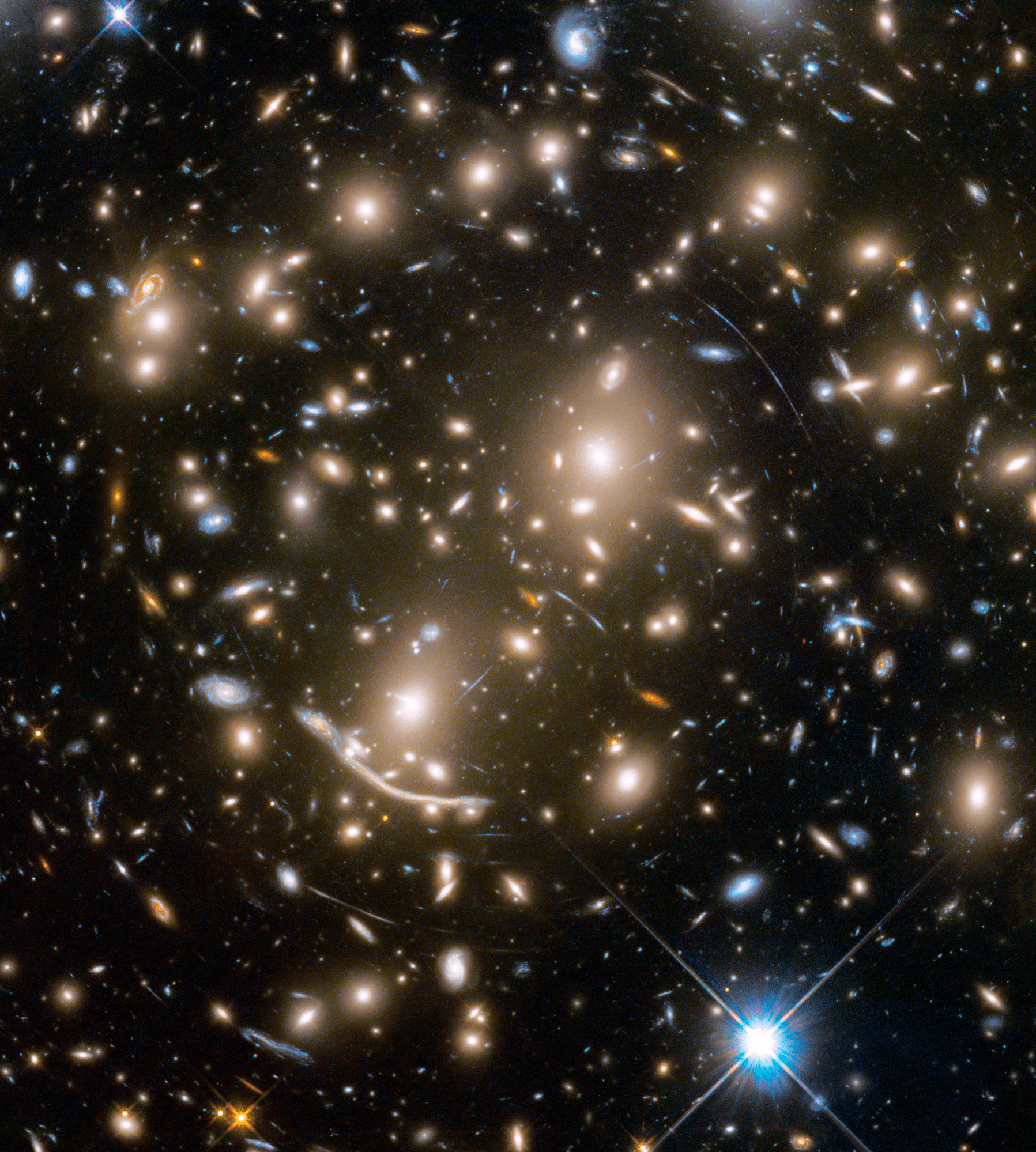 A packed field of galaxies and curved blue streaks and arcs. Bright blue-white foreground star at bottom right.
