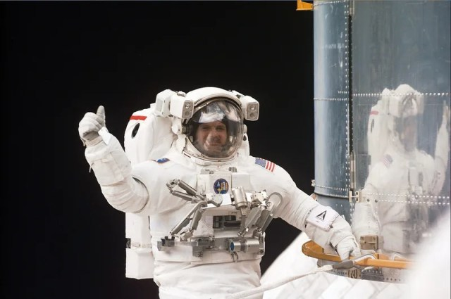 Astronaut in a white space suit tethered to the Hubble Space Telescope floating in space.