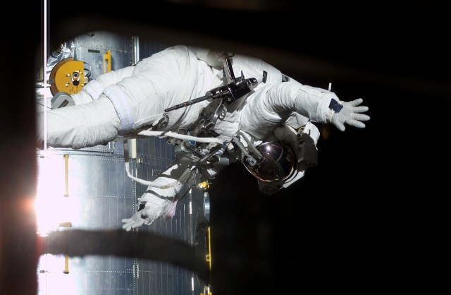 Astronaut in white space suit waving to the camera outside of the Hubble Space Telescope floating in space.