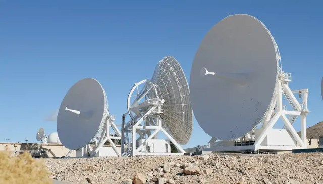 Three large white antennas in the desert with a blue sky in the background