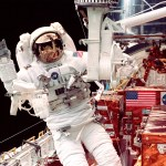 Astronaut on an EVA in a white space suit waving while working on the Hubble space telescope.