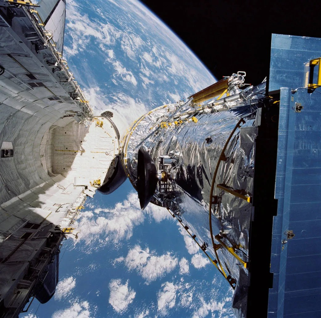 Hubble Space Telescope being deployed in space from the the shuttle Discovery's cargo bay, the Earth in the background.