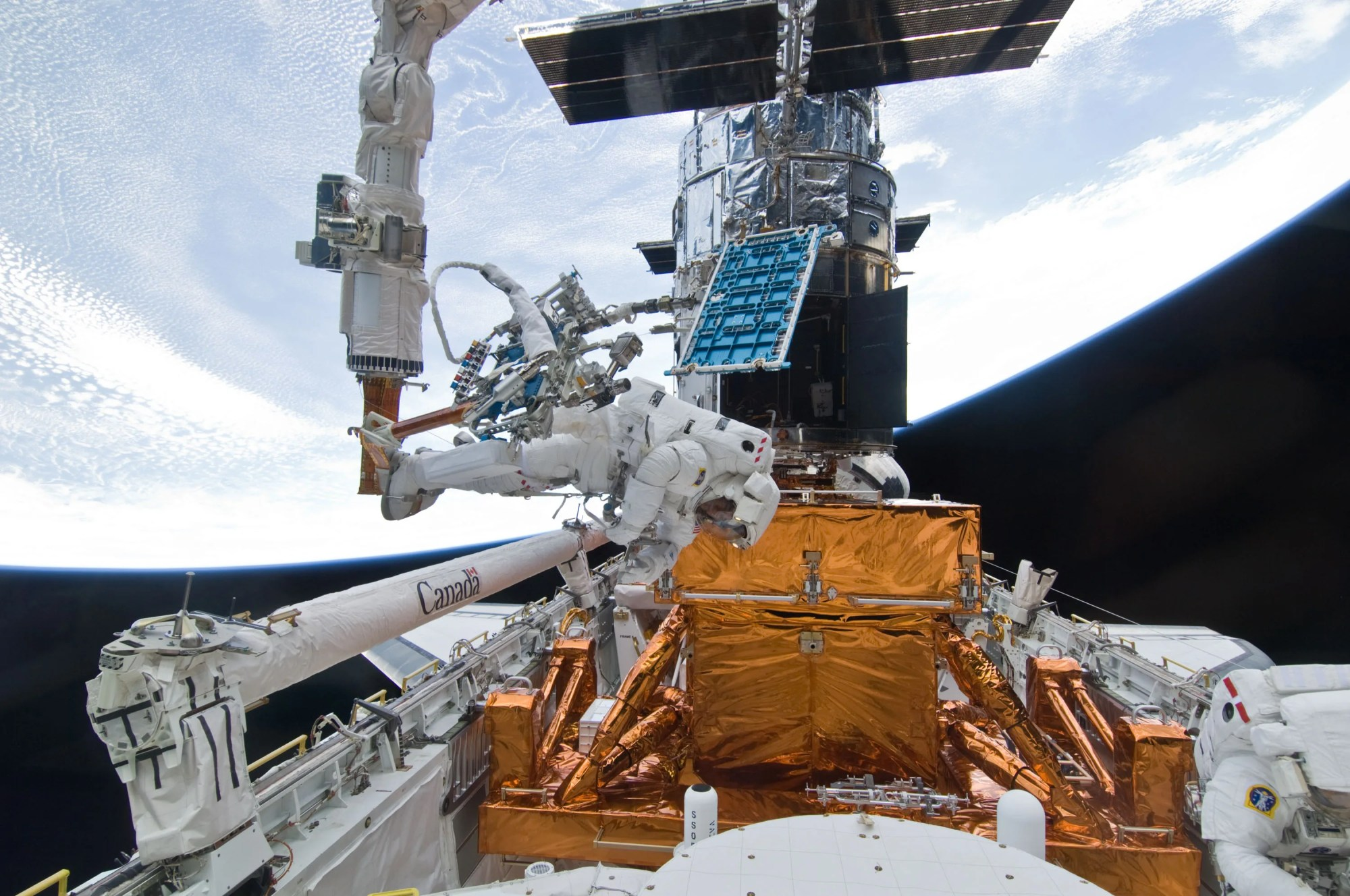 Two astronauts in white space suits on an EVA working to maintain the Hubble Space Telescope.