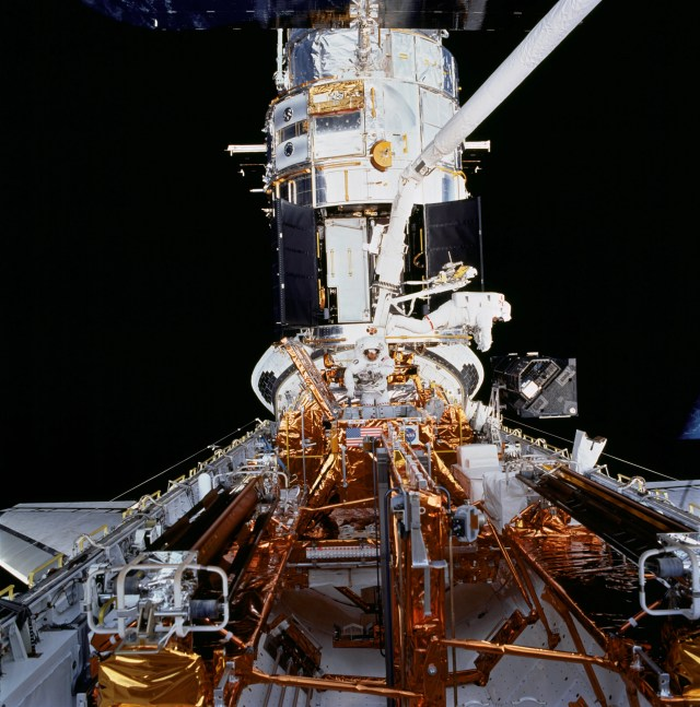 Two astronauts in white space suits in the space shuttle bay replacing instruments on Hubble in space