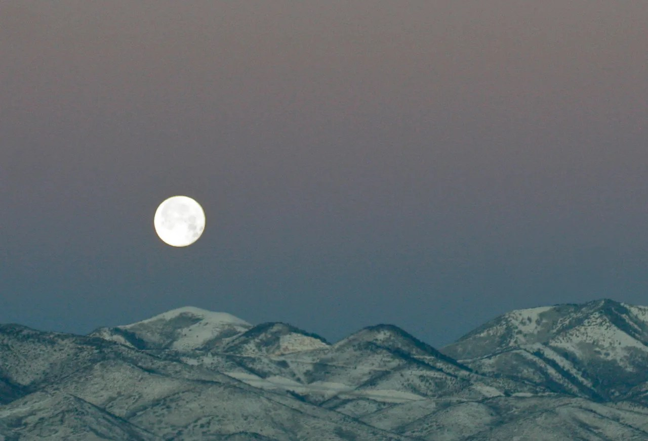 full moon setting over mountains
