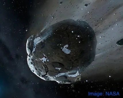 A big, slightly oblong, dark and light grey asteroid is moving from the upper right to the lower left, shedding smaller chunks of material and a cloud of dust.