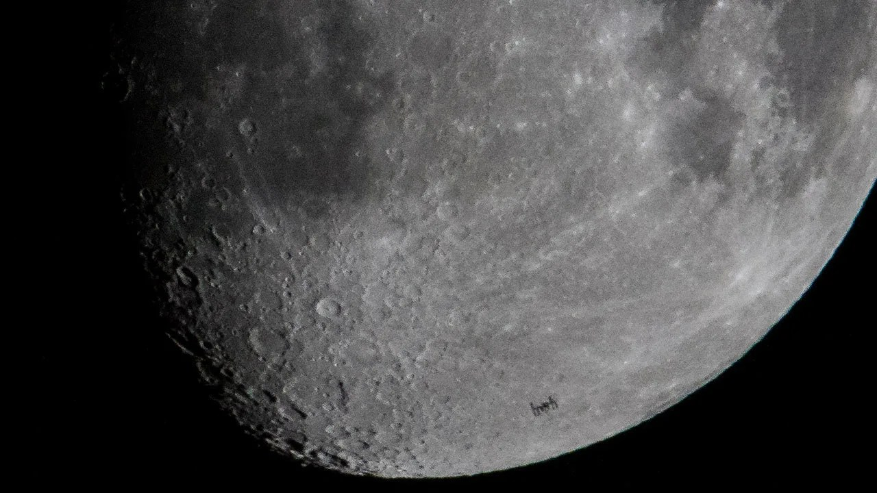 Close of image of moon with a small silhouette of the space station on the lower third.