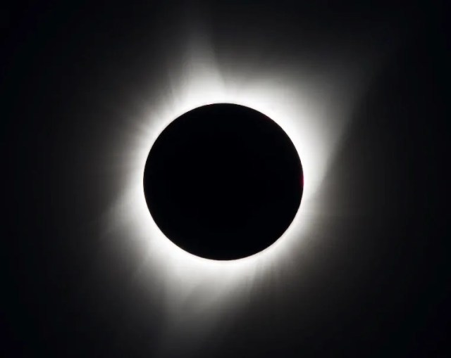 A black circle representing the Moon, surrounded by bright light from the Sun's atmosphere