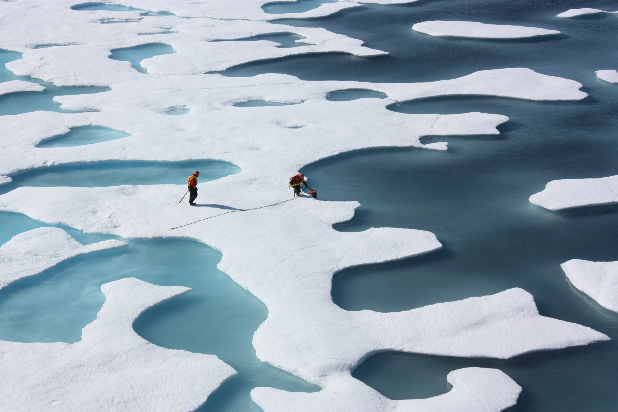 Science crew members retrieve a canister from melt ponds on the Arctic Ocean.