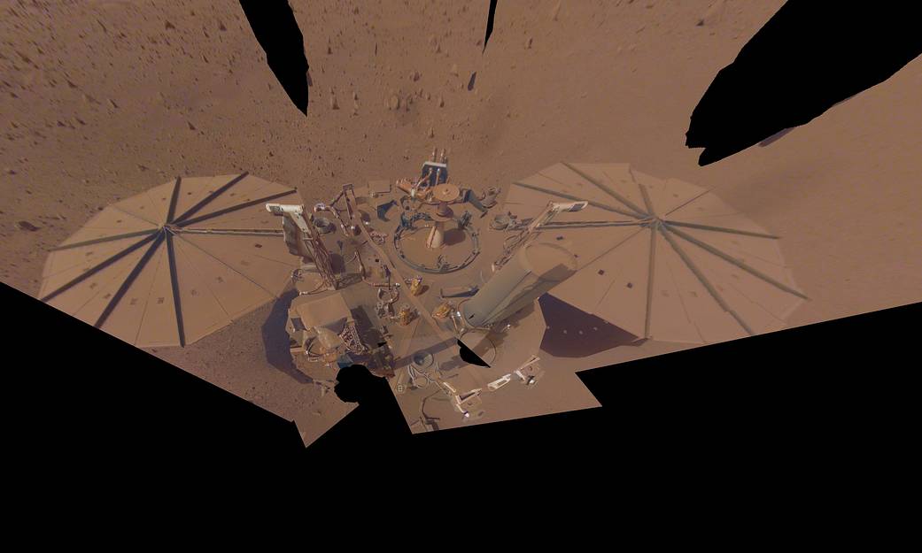 Selfie photo of red-dust covered lander showing the top and its solar panels
