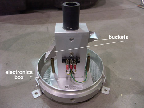 The insides of a tipping bucket rain gauge are shown here. The rain enters through the black pipe on top and fills one of two triangular buckets, here, the one on the right. When it fills to 1/100th of an inch, the bucket tips downward, raising the bucket on the left to collect rain. Below the buckets (not pictured, but inside the gray compartment), is a magnet that swings and completes a circuit that records the data onto the computer. Credit: Kara Prior