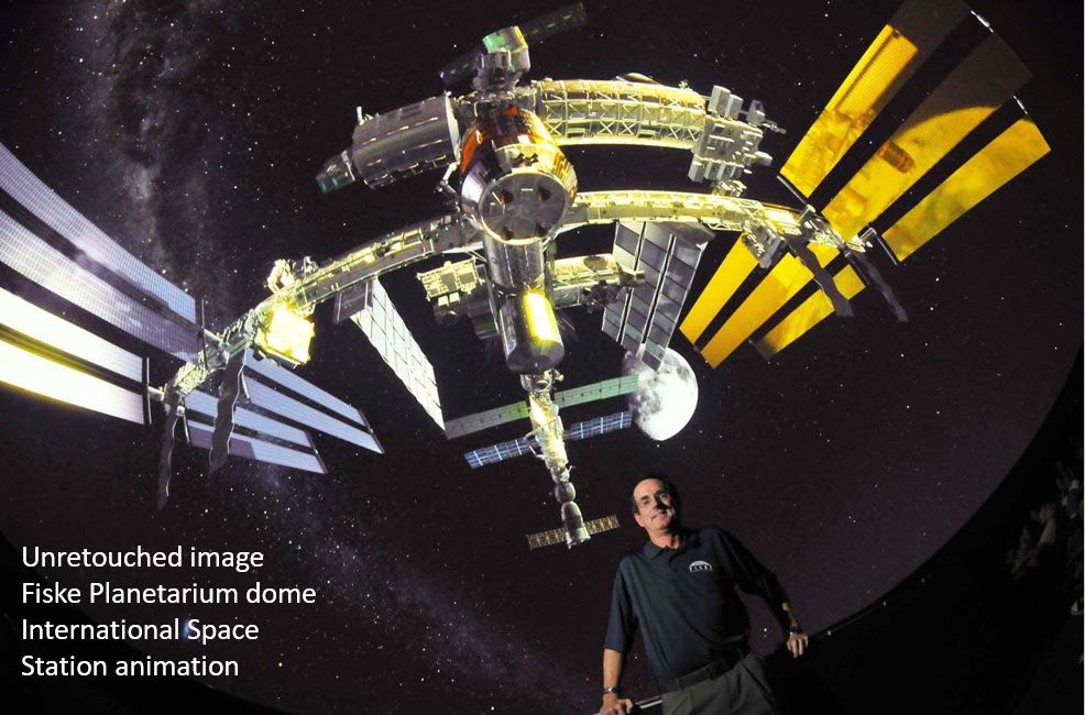 Doug Duncan is standing in a planetarium with a massive image of the International Space Station projected on the dome above him.